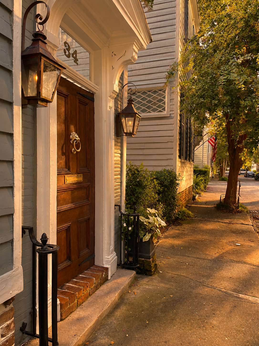 Historic Charleston front door with gas lanterns on a tree-lined sidewalk at golden hour